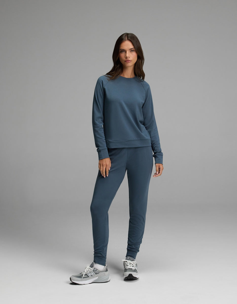 A woman stands against a plain gray background wearing the Cozy Earth Women’s Brushed Bamboo Jogger Set in Dawn with gray sneakers, looking at the camera with a neutral expression.