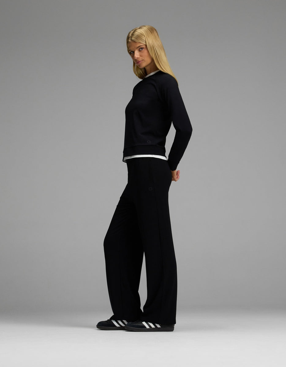 A woman with straight blonde hair stands in profile against a gray background, wearing the Cozy Earth Women’s Brushed Bamboo Wide Leg Pull On Pant & Pullover Crew Set in black.