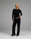 A woman with blonde hair models the Cozy Earth Women’s Brushed Bamboo Wide Leg Pull On Pant & Pullover Crew Set in black, paired with black shoes. She stands in a neutral pose against a plain gray background.|Color:Black