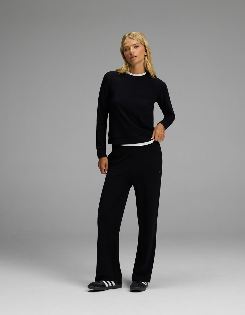 A woman with blonde hair models the Cozy Earth Women’s Brushed Bamboo Wide Leg Pull On Pant & Pullover Crew Set in black, paired with black shoes. She stands in a neutral pose against a plain gray background.