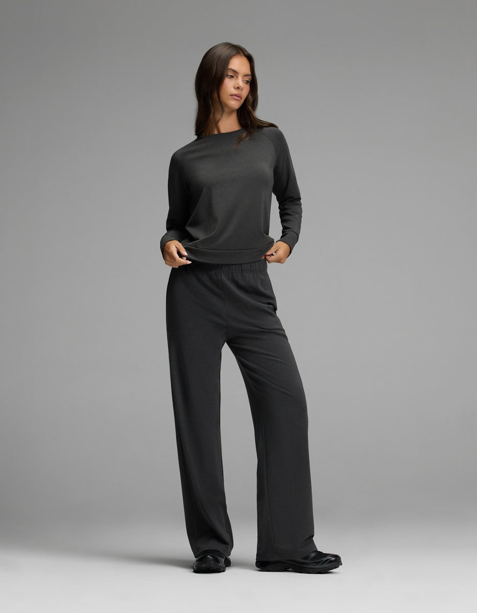 A woman stands in a relaxed pose against a plain gray background, wearing the Cozy Earth Women’s Brushed Bamboo Wide Leg Pull On Pant & Pullover Crew Set in charcoal.