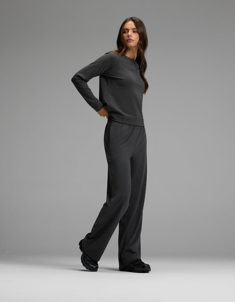 A woman with long brown hair wears the Cozy Earth Women’s Brushed Bamboo Wide Leg Pull On Pant & Pullover Crew Set in dark grey, paired with black shoes, standing against a plain light grey background.