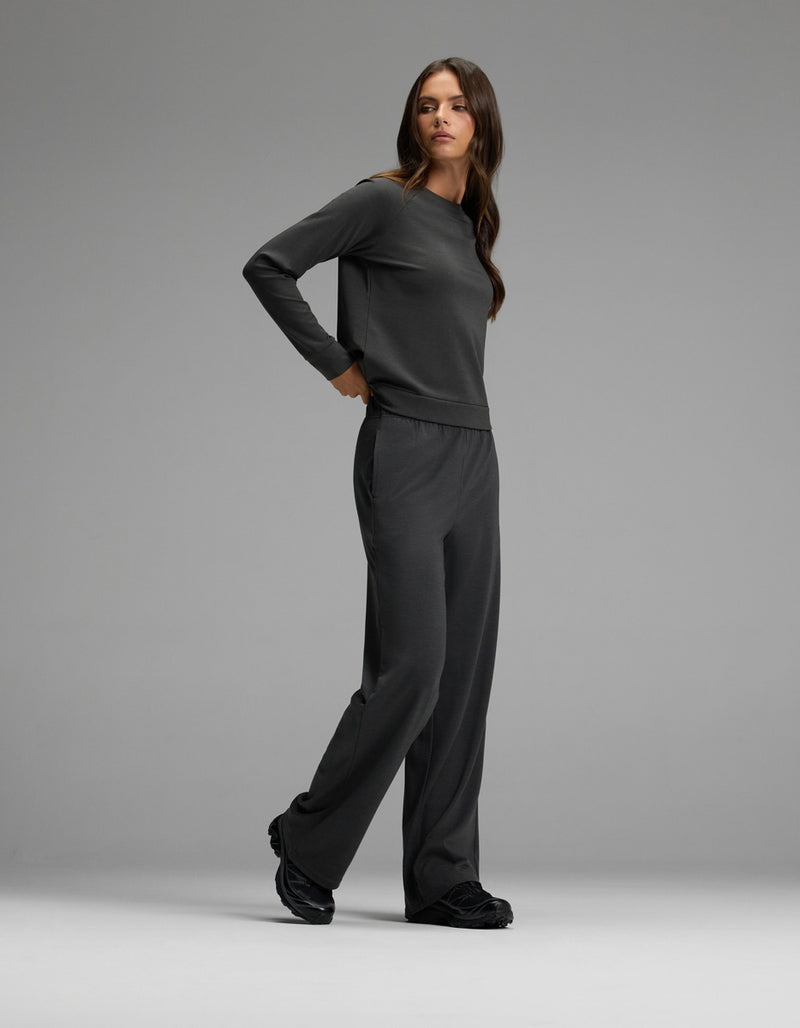 A woman with long brown hair wears the Cozy Earth Women’s Brushed Bamboo Wide Leg Pull On Pant & Pullover Crew Set in dark grey, paired with black shoes, standing against a plain light grey background.