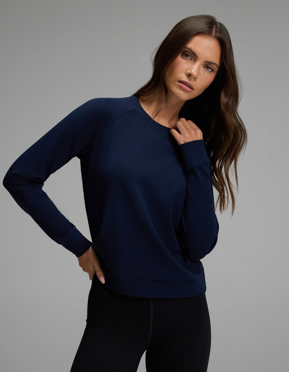 A woman with long brown hair wears the Cozy Earth Women’s Brushed Bamboo Pullover Crew in navy blue, paired with black leggings, standing against a plain gray background.|Color:Navy