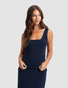 A woman with long brown hair, wearing Cozy Earth's Women's Brushed Bamboo Square Neck Tank in navy blue, stands against a light gray background, smiling softly as she looks slightly to her left.|Color:Navy