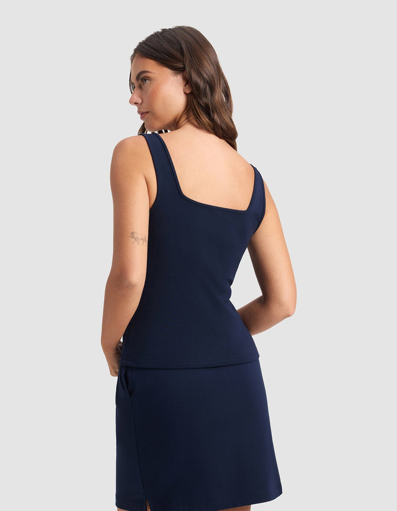 A woman with long brown hair wears the Cozy Earth Women's Brushed Bamboo Square Neck Tank in navy blue, facing slightly away to highlight its square neckline and shoulder straps, set against a plain light gray background.