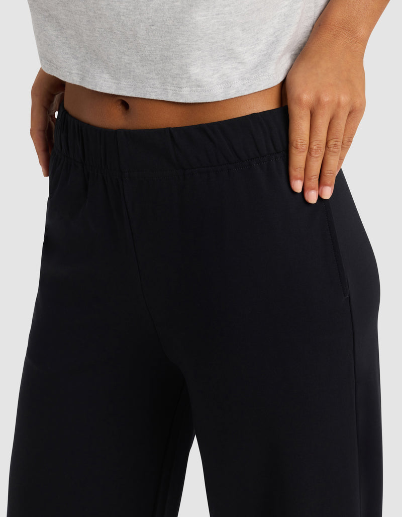A woman models the Cozy Earth Women's Brushed Bamboo Wide Leg Pull-On Pant in black, standing with one hand on her hip to display the waistband and side pocket, paired with a light gray cropped top.