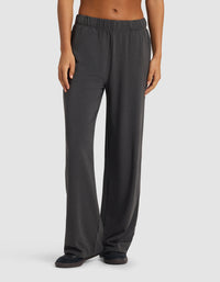 A person models the Cozy Earth Women's Brushed Bamboo Wide Leg Pull-On Pant in dark gray with black slippers, standing against a plain light gray background. Only the lower torso and legs are visible.|Color:Charcoal