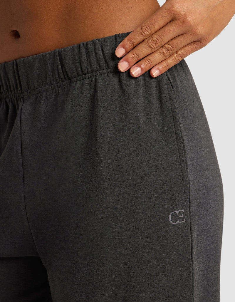 A close-up of a hand resting on the waistband of Cozy Earth's Women's Brushed Bamboo Wide Leg Pull-On Pant in dark gray, featuring an elastic band and a small "CE" logo on the hip against a plain light-colored background.