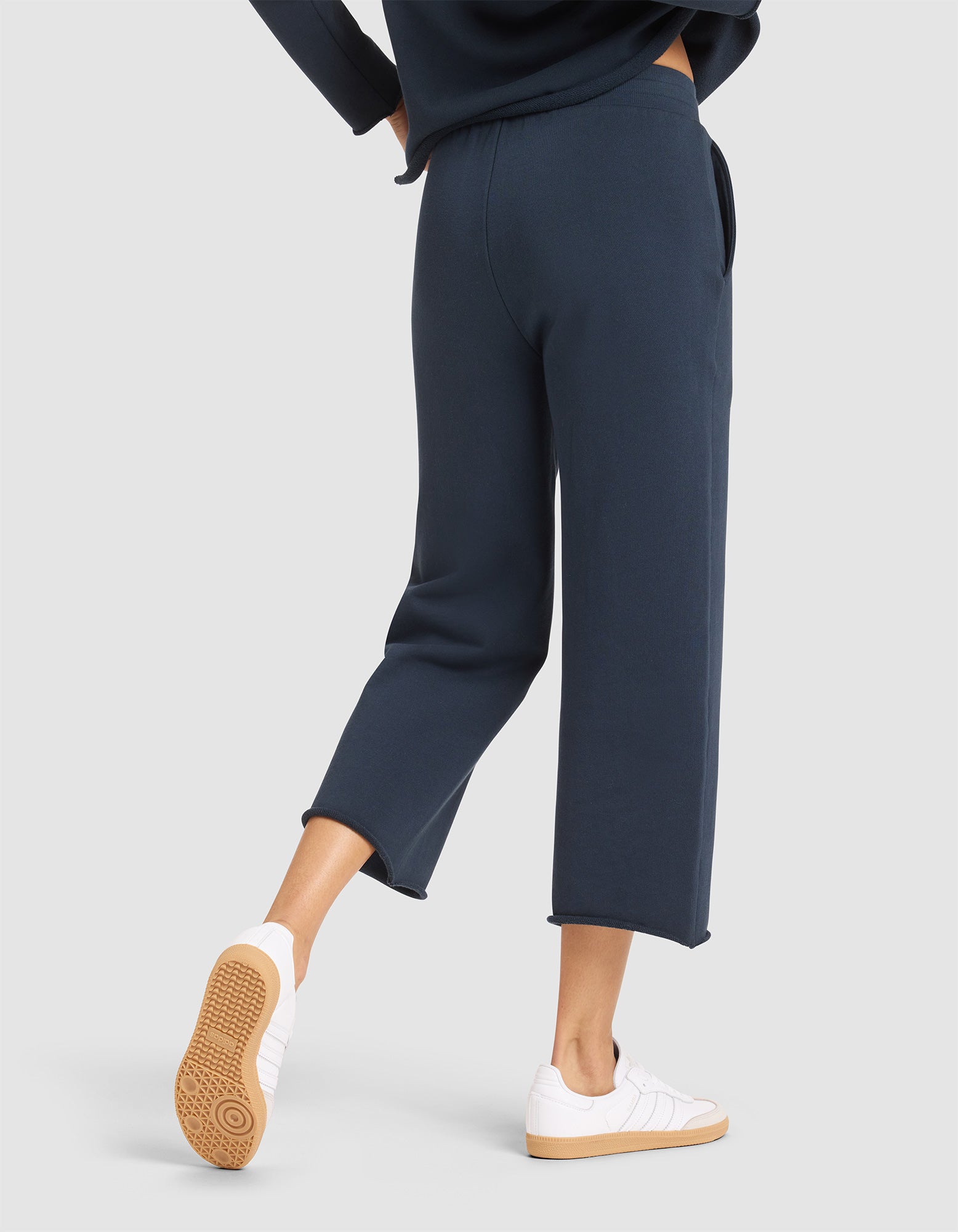 A person wearing Cozy Earth’s Women's Chelsea Cropped Pant in navy and white sneakers is shown from the back walking forward, with the lower half of their body highlighted against a plain background. 