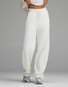 A person stands against a plain gray background wearing the Cozy Earth Women’s Chelsea Pant in Bone and a white cropped top, paired with gray sneakers. Their face is not visible.|Color:Bone