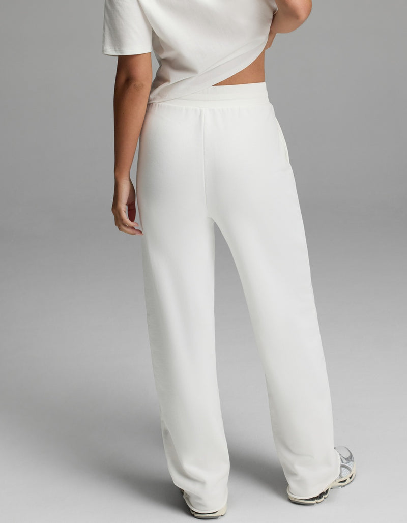 A person, visible from the waist down, is wearing Cozy Earth’s Women’s Chelsea Pant in white. The background is plain gray.