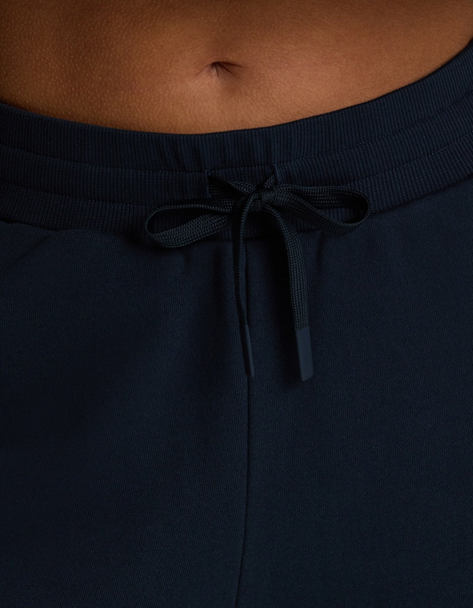 Close-up of a person’s lower torso wearing Cozy Earth Women’s Chelsea Pant in dark navy, featuring a visible tied bow at the waistband and part of the person’s belly button showing above the pants.