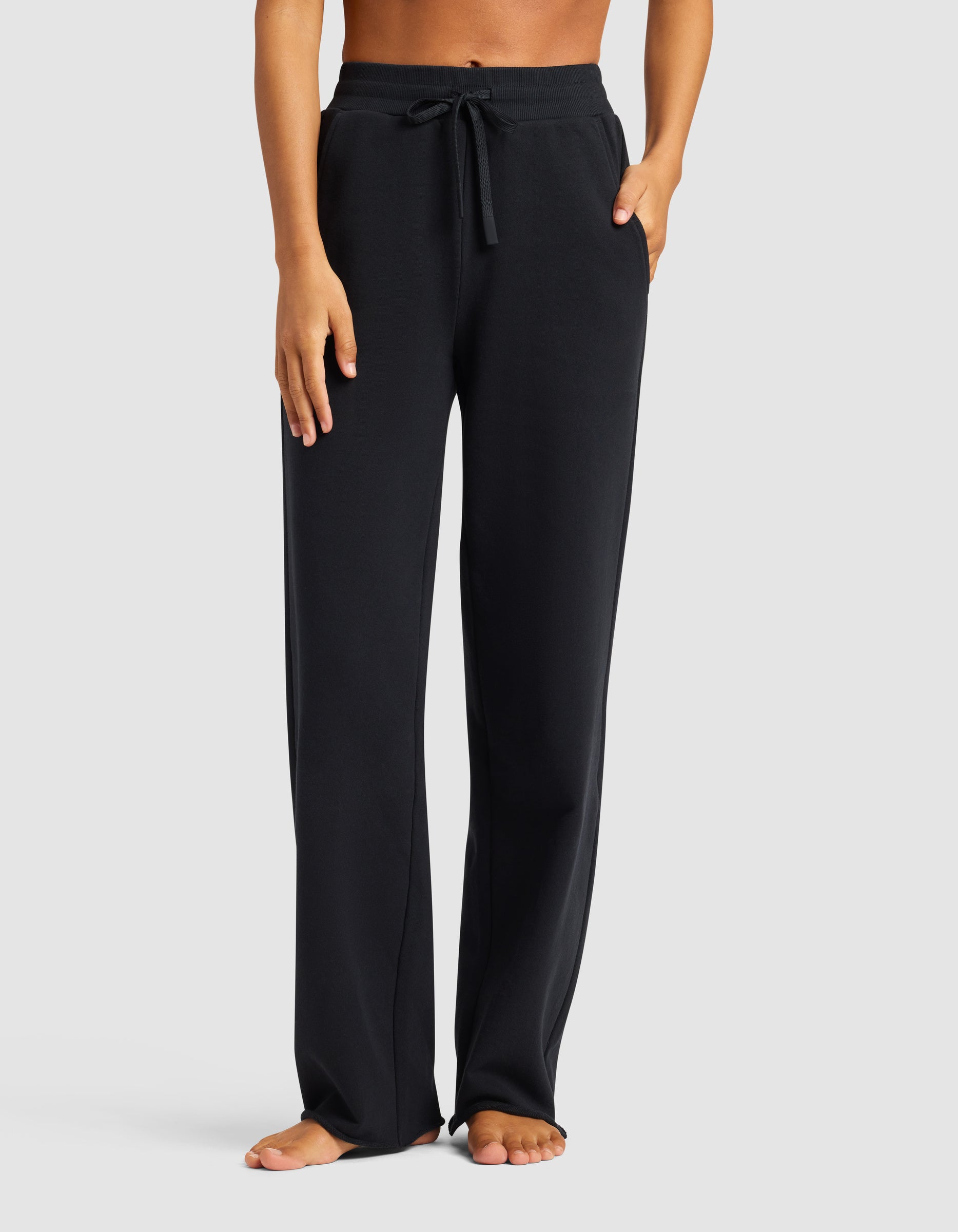 A person wears the Cozy Earth Chelsea Pant—black, loose-fitting with a drawstring waist and pockets—standing barefoot from shoulders down against a plain light background.|Color:Jet Black