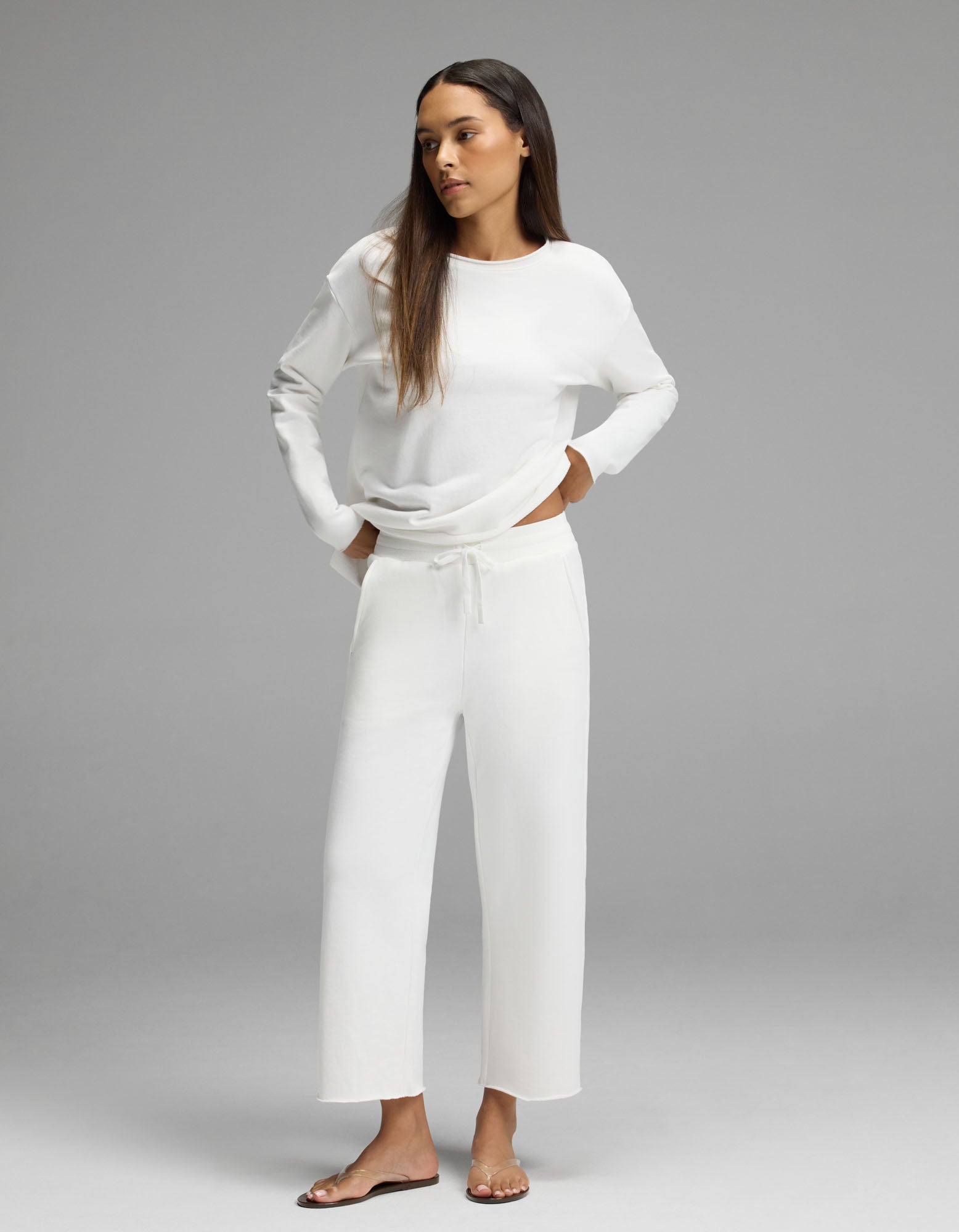 A woman models the Cozy Earth Women’s Chelsea Cropped Set in Bone, standing with her hands in her pockets and looking to the side against a plain gray background.|Color:Bone