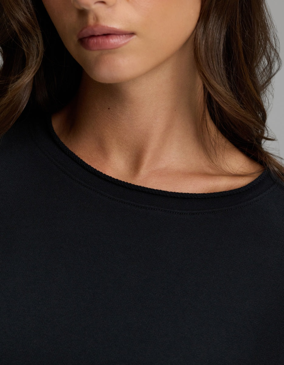 A close-up of a woman wearing the Cozy Earth Women’s Chelsea Pullover in black, showing her neck, part of her face, and wavy brown hair.