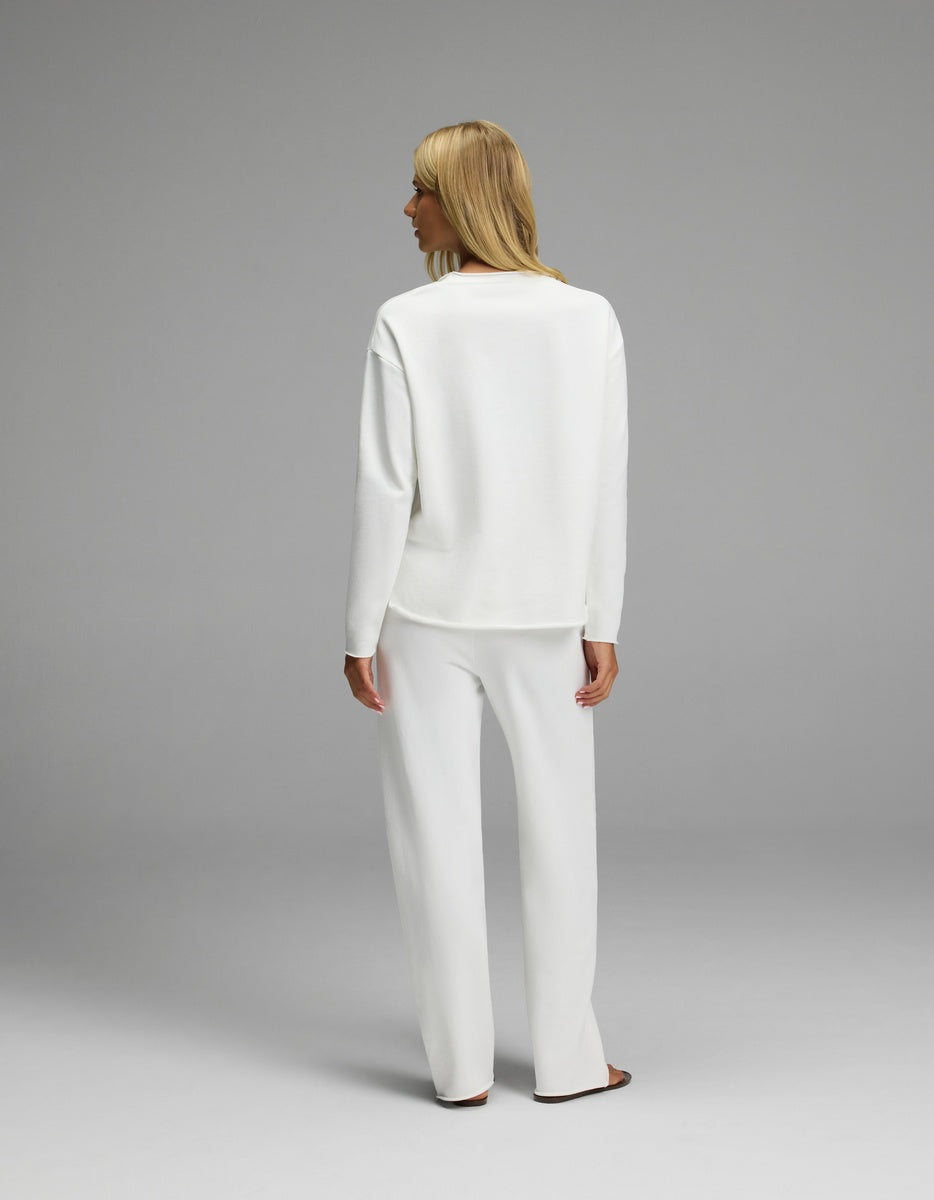 A person with blonde hair, seen from behind, is wearing the Cozy Earth Women’s Chelsea Set—a loose-fitting white long-sleeve top paired with matching wide-leg pants. The background is plain and light gray.