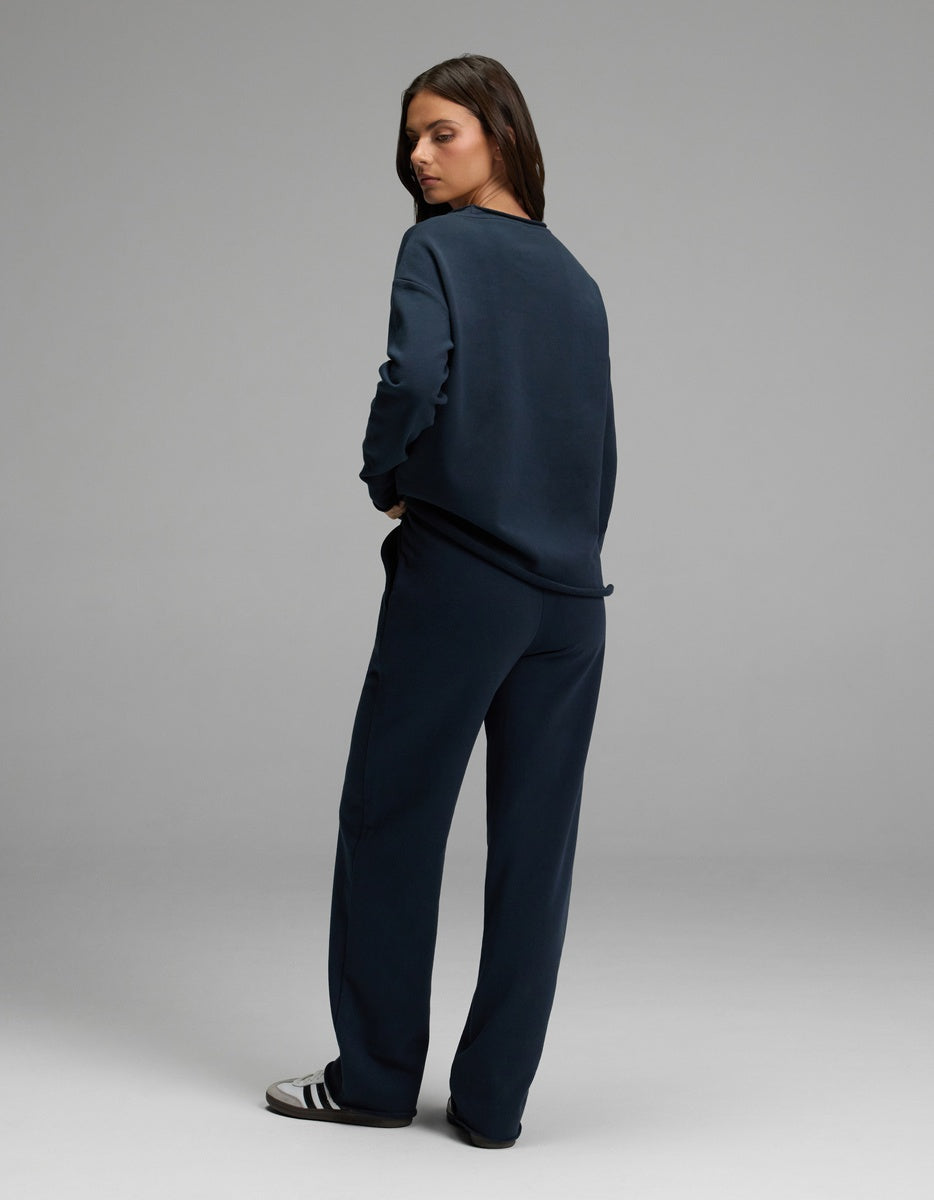 A woman stands in a relaxed pose against a plain gray background, wearing the Cozy Earth Women’s Chelsea Set in navy blue, paired with black and white sneakers.