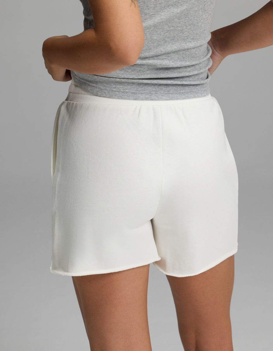 A person, seen from behind with hands on hips, is wearing Cozy Earth’s Women’s Chelsea Short in white and a gray sleeveless top against a plain light gray background.|Color:Bone