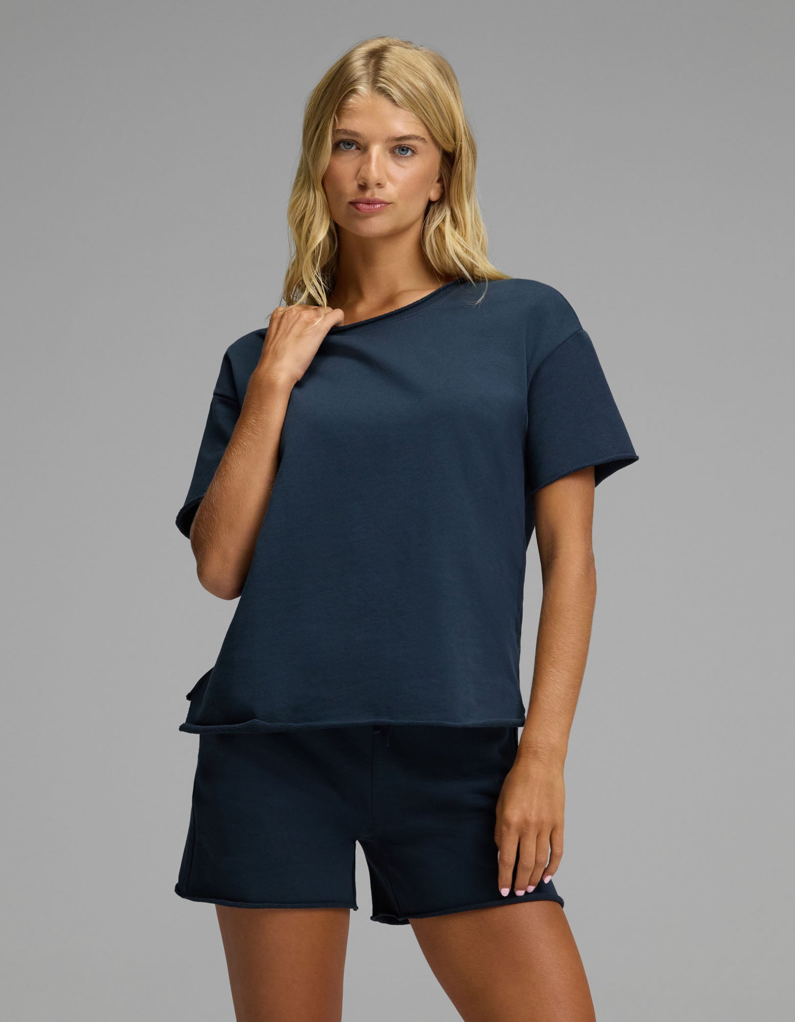 A woman with blonde hair wears the Cozy Earth Women’s Chelsea Short Sleeve Set in Eclipse, standing against a plain gray background and looking at the camera with a relaxed expression.