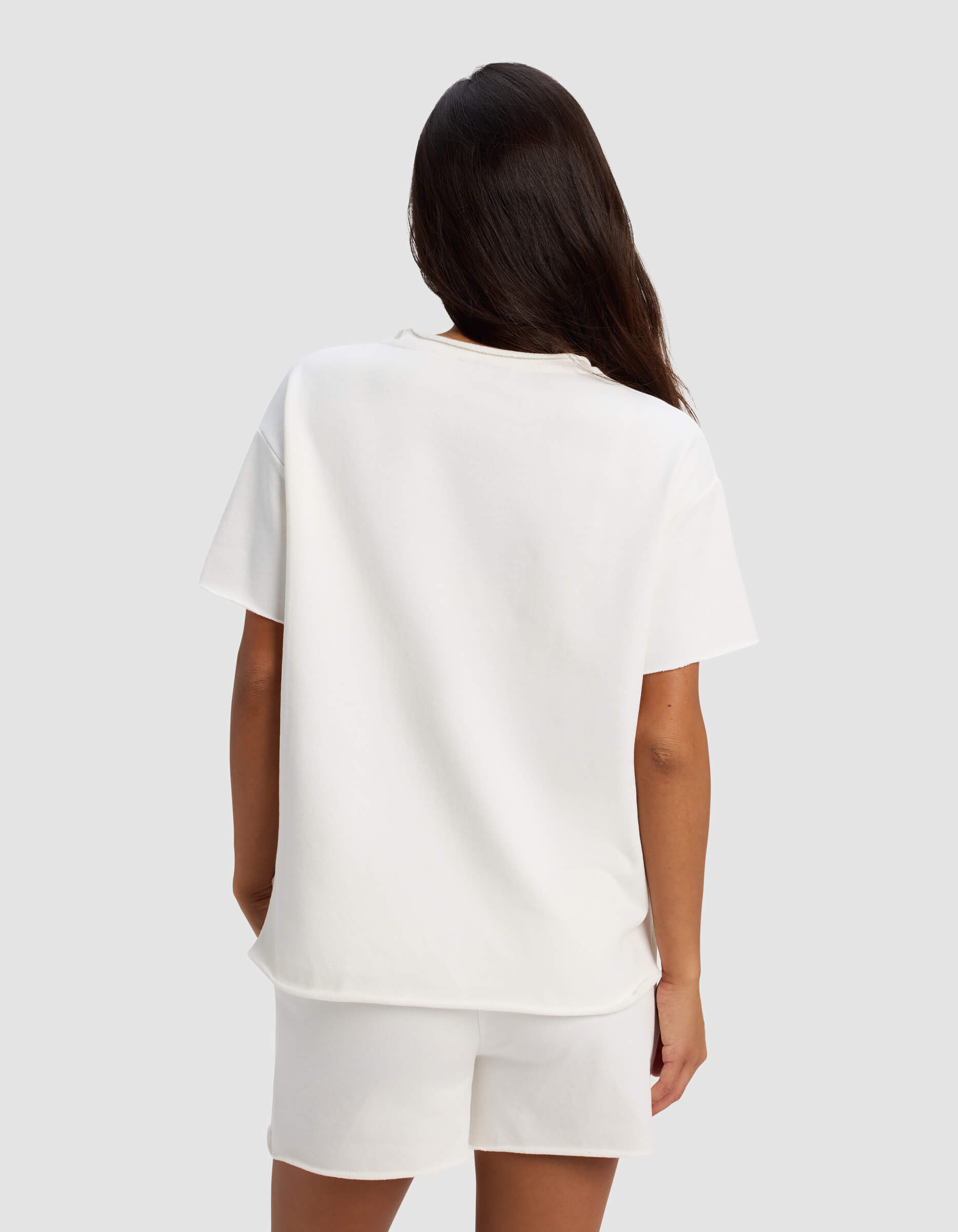 A woman with long dark hair, seen from behind, wears the Cozy Earth Women's Chelsea Short Sleeve and white shorts against a plain light gray background.|Color:Bone