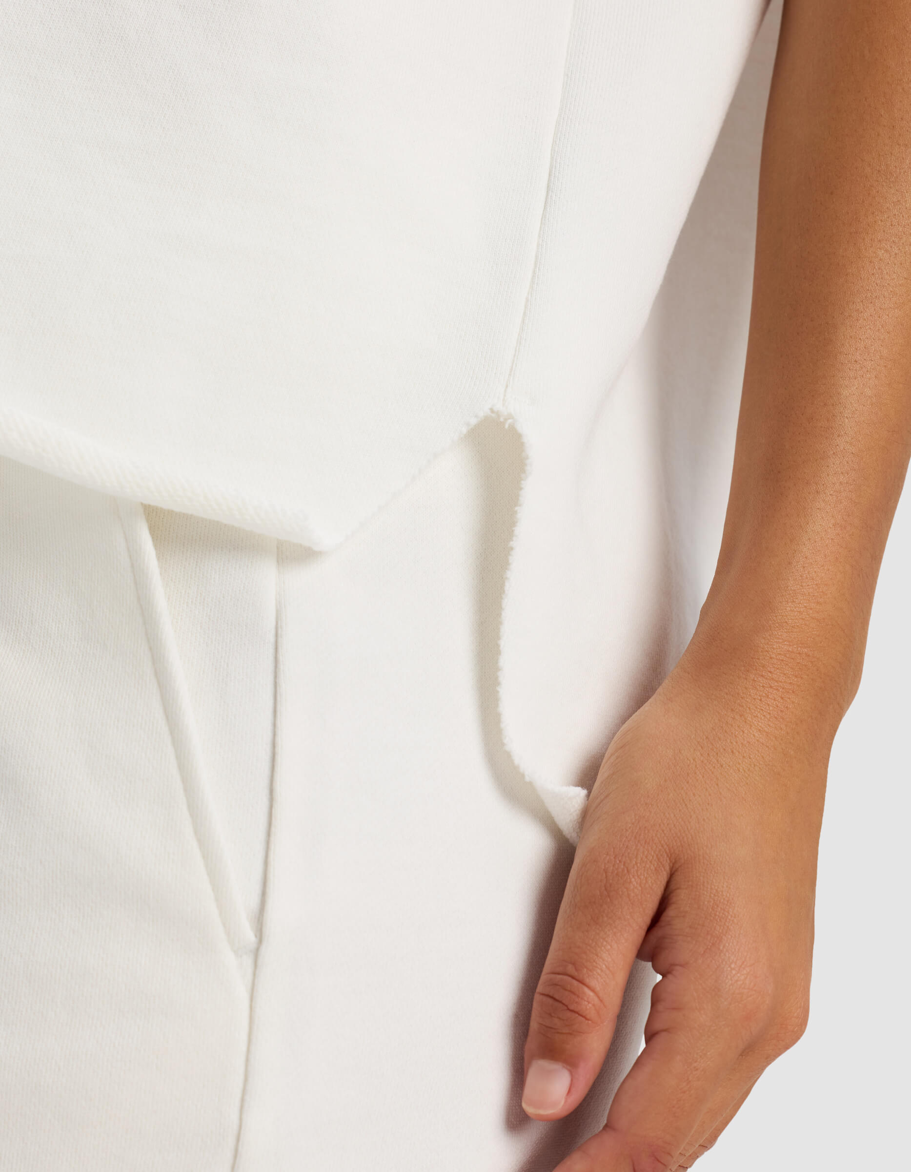 A close-up of a person’s hand on their hip, wearing the Cozy Earth Women’s Chelsea Short Sleeve in white, featuring soft-textured layered fabric and visible seams. The person has a medium-light skin tone.
