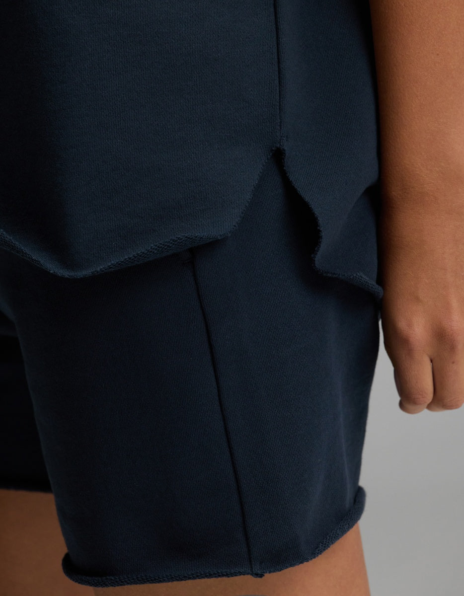 A close-up of a person’s hand resting by their side, wearing the Cozy Earth Women’s Chelsea Short Sleeve top in dark blue paired with matching shorts featuring raw, unfinished edges.