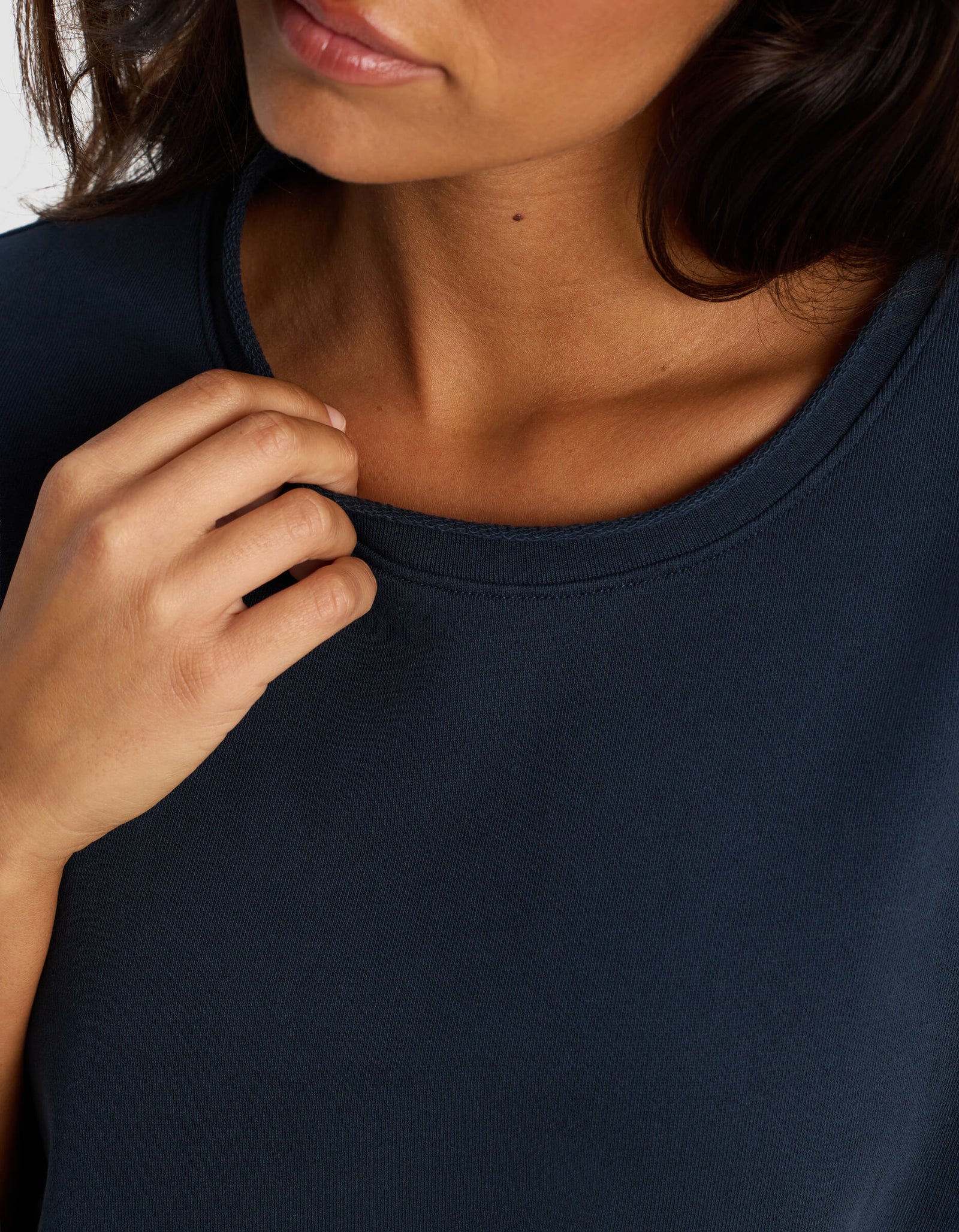 A close-up shows a woman wearing the Cozy Earth Women's Chelsea Short Sleeve in dark navy blue, gently holding the neckline with her left hand. Only her lower face, neck, and upper chest are visible.