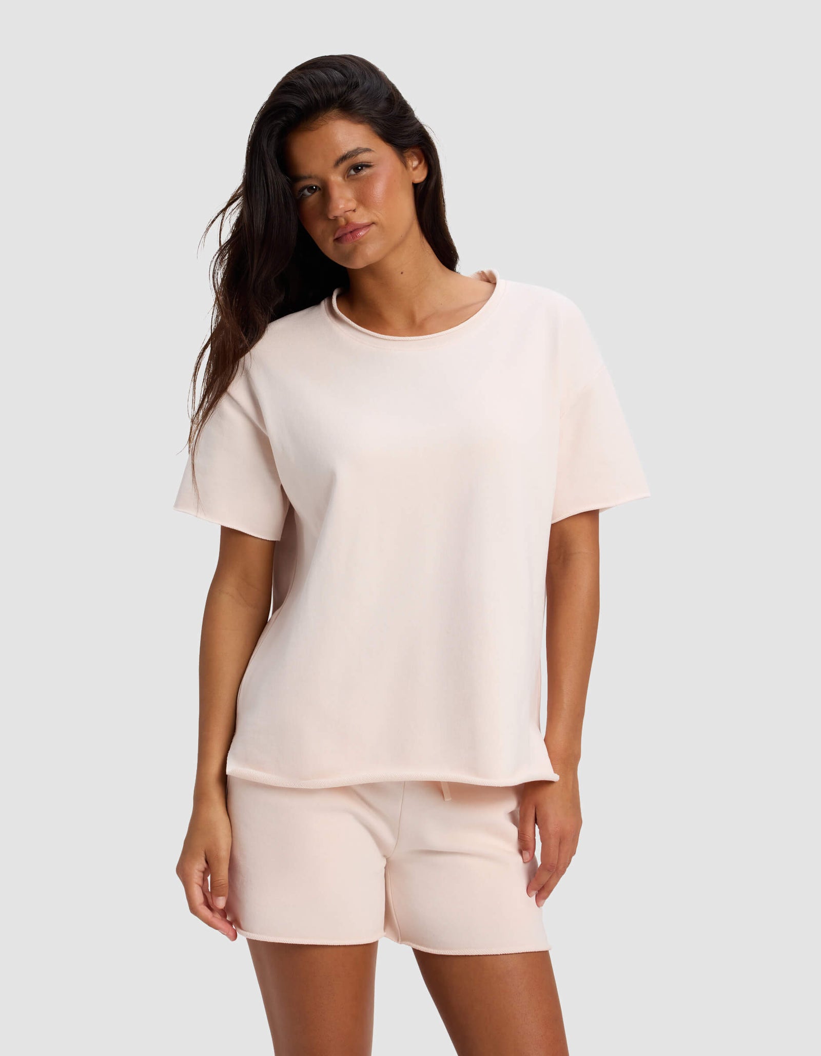 A woman models the Cozy Earth Women's Chelsea Short Sleeve and matching shorts in light pink, standing against a plain light gray background with a relaxed expression.