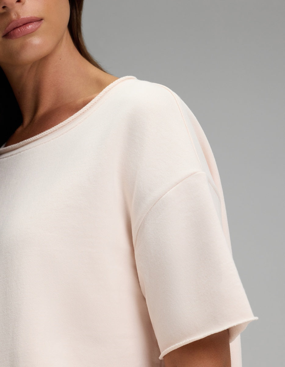 A woman is shown from the shoulders up, her face partially out of frame, wearing the Cozy Earth Women’s Chelsea Short Sleeve in light beige against a plain gray background.