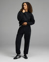A person with curly hair wears the Women’s CityScape Crewneck & Sweatpant Set by Cozy Earth, standing in a relaxed pose against a plain gray background.|Color:Jet Black