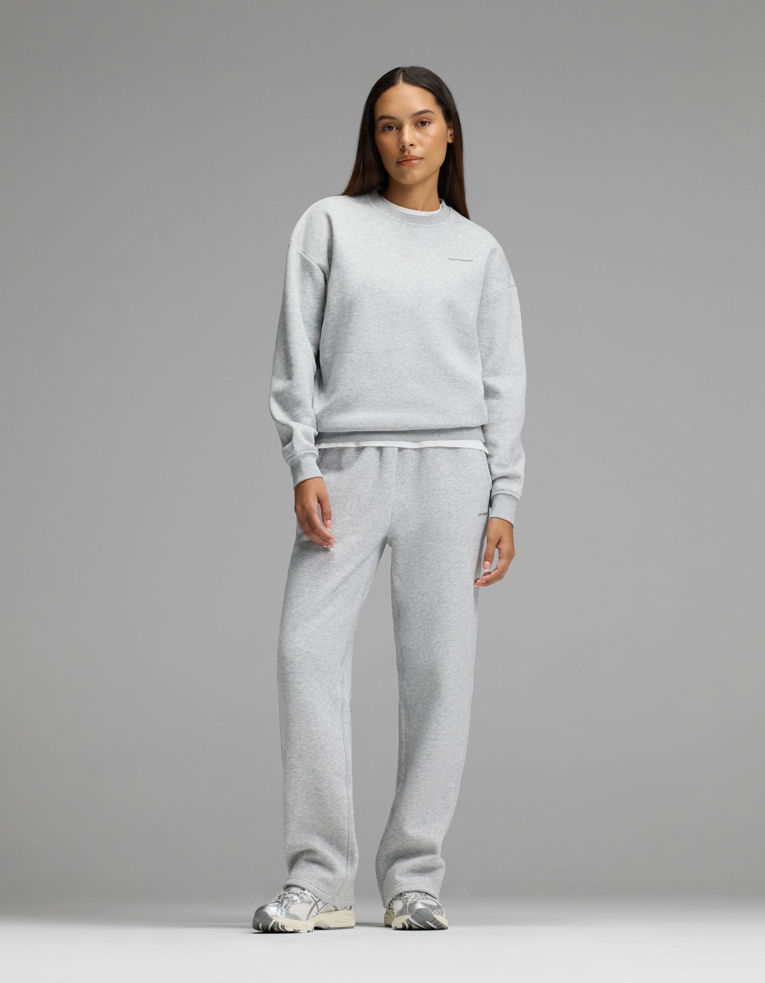 A woman stands facing forward against a plain gray background, wearing Cozy Earth’s Women’s Cityscape 2.0 Crewneck & Wide Leg Pant Set in Heather Grey, paired with silver sneakers.|Color:Heather Grey