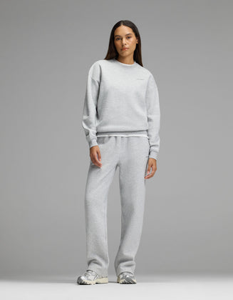 A woman stands facing forward against a plain gray background, wearing Cozy Earth’s Women’s Cityscape 2.0 Crewneck & Wide Leg Pant Set in Heather Grey, paired with silver sneakers.|Color:Heather Grey