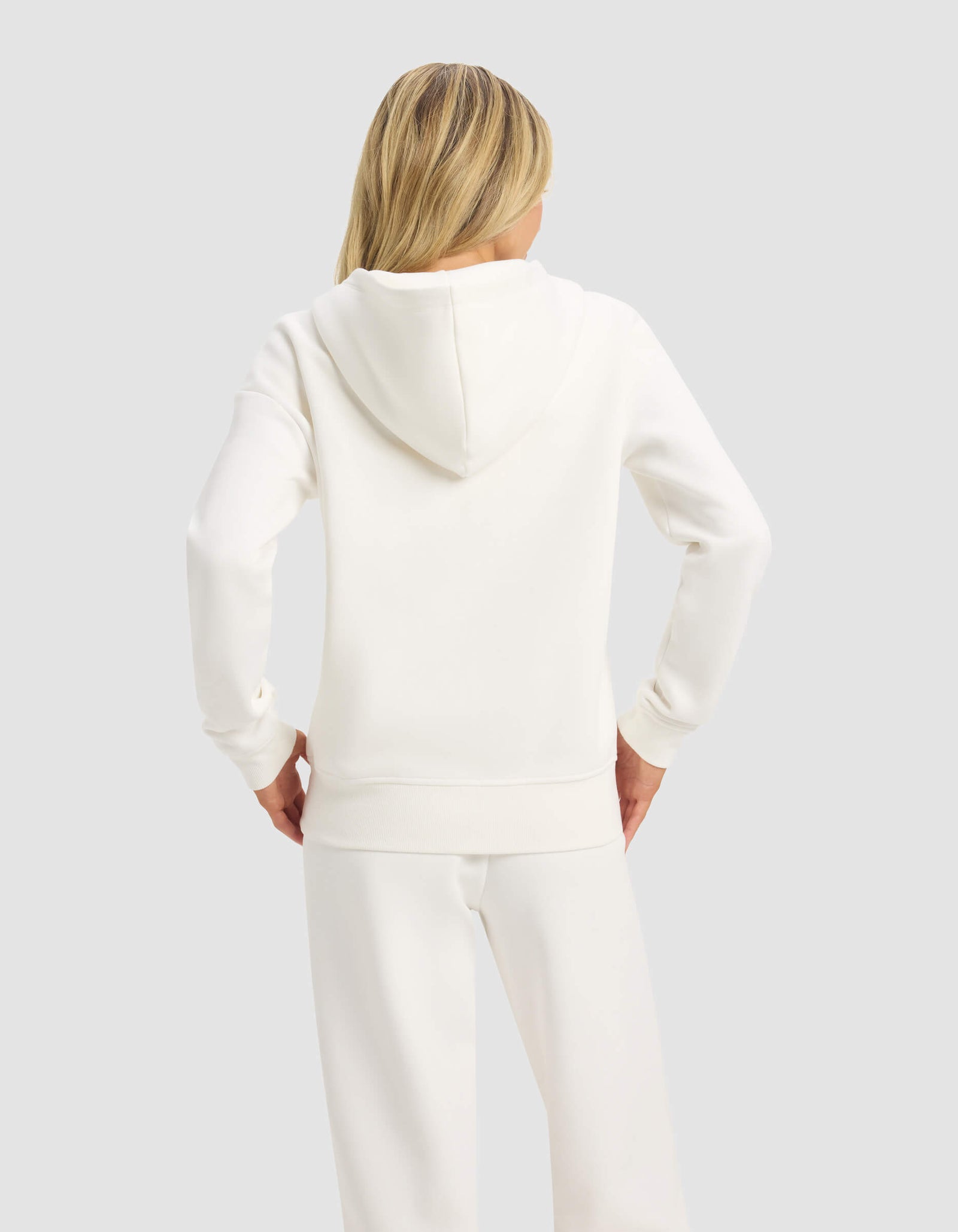 A person with long blonde hair models the Cozy Earth Women's CityScape 2.0 Full Zip sweatshirt, shown from the back in white against a plain, light gray background.