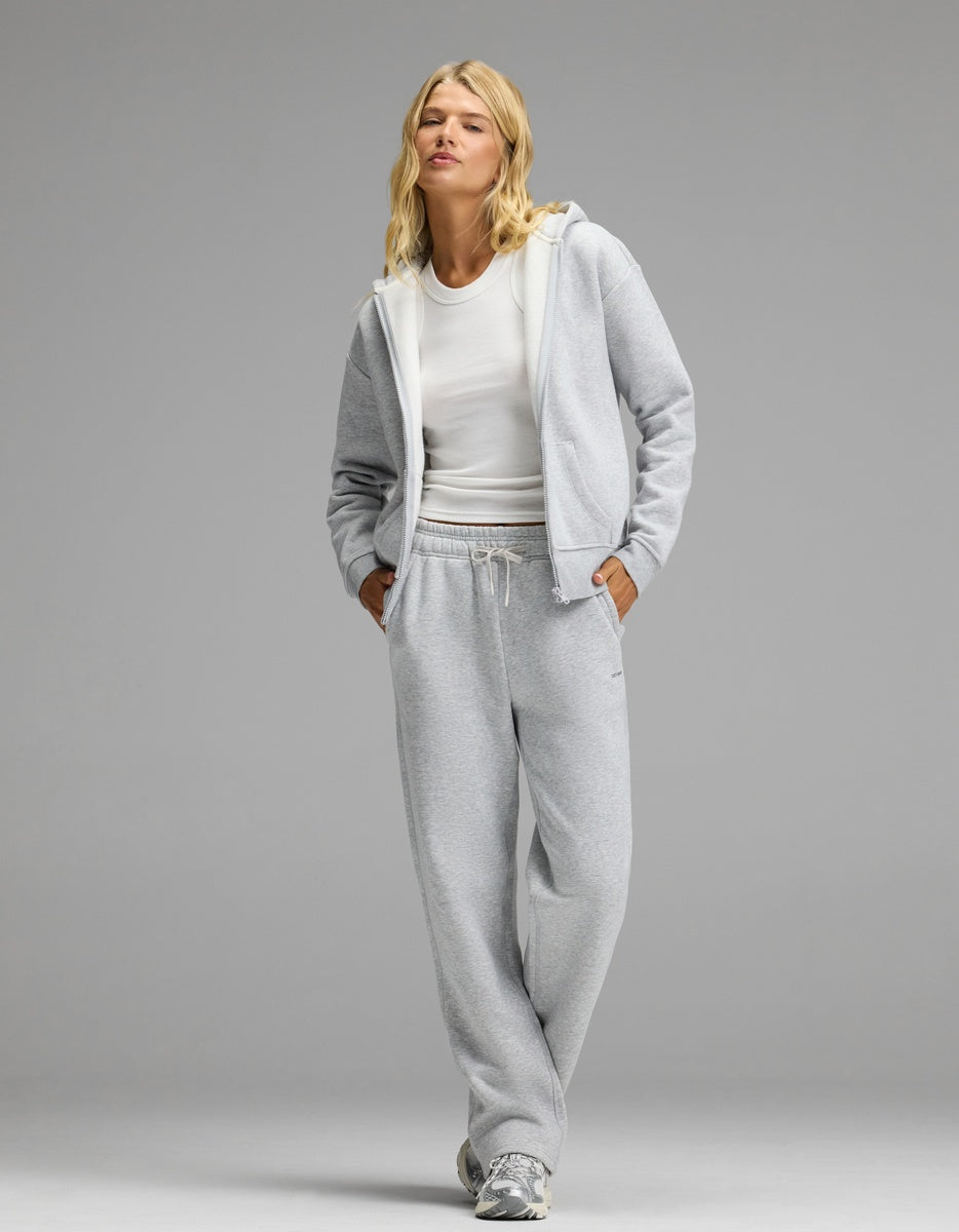 A model wears a grey Cozy Earth Women’s Cityscape Full-Zip Hoodie & Wide Leg Pant Set over a white tank top, paired with sneakers.