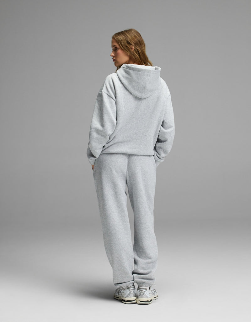 A woman models the Cozy Earth Women’s CityScape Hoodie & Sweatpant Set in light gray, standing with her back to the camera and hands in her pockets against a plain gray background.