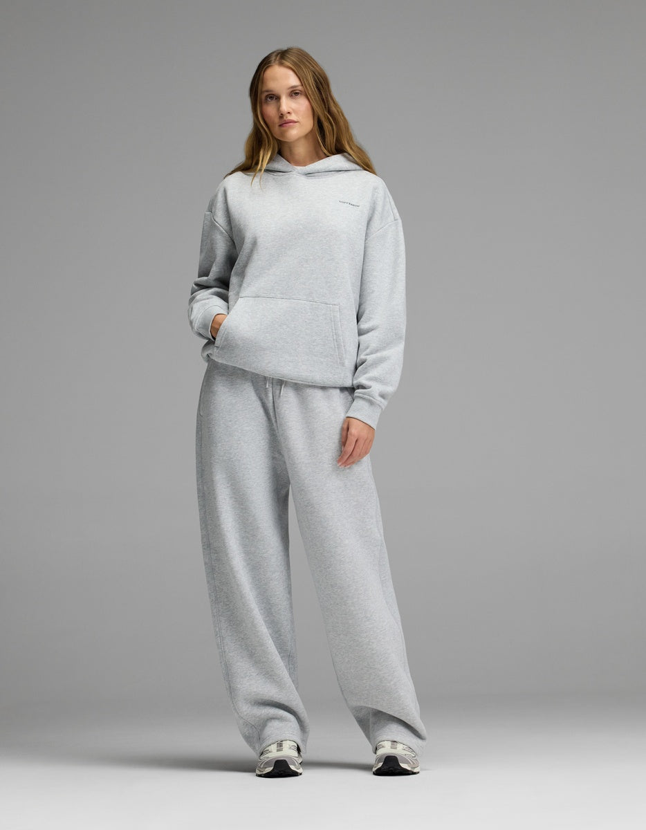A person stands against a gray background, wearing the Cozy Earth Women’s CityScape Hoodie & Wide Leg Pant Set with white sneakers.