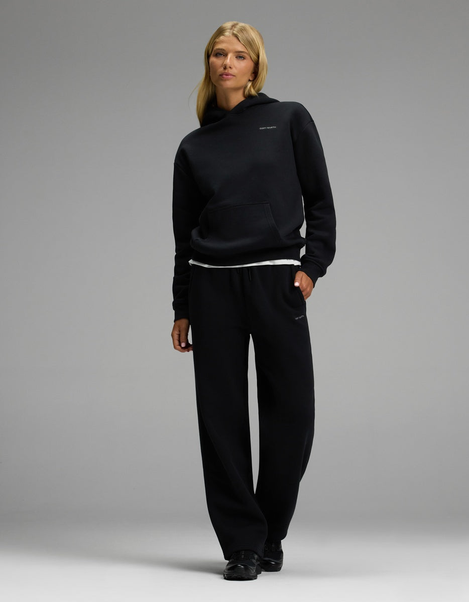 A woman models the Cozy Earth Women’s CityScape Hoodie & Wide Leg Pant Set with black shoes, one hand in her pocket, looking at the camera against a simple background.