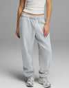 A person models the Cozy Earth Women’s CityScape Sweatpant in light gray, featuring a drawstring waist, paired with a white tank top and silver athletic shoes against a plain gray background. Only the lower half of the body is visible.|Color:Heather Grey