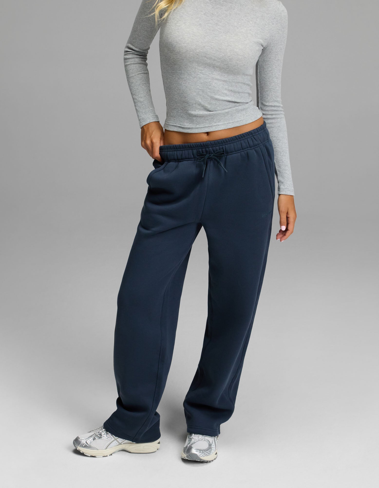 A person wearing a fitted gray long-sleeve top, Cozy Earth’s Women’s Cityscape 2.0 Wide Leg Pant in Eclipse, and white sneakers stands against a plain gray background.|Color:Eclipse