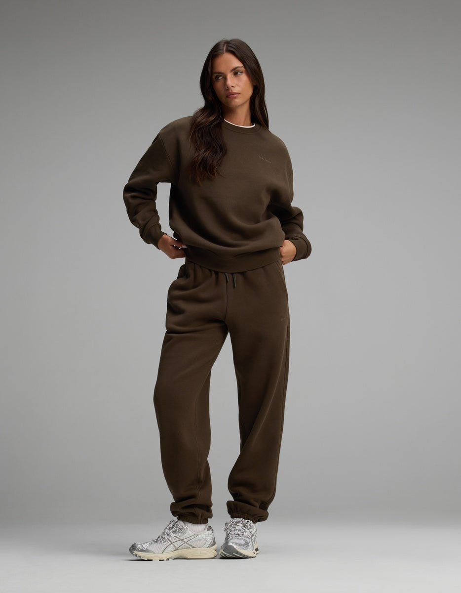 A person wears a dark brown Cozy Earth Women’s CityScape Crewneck and matching sweatpants with white athletic shoes.