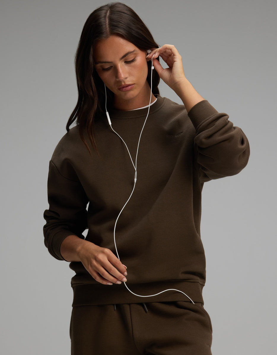 A person wearing a dark olive green Women’s CityScape Crewneck adjusts their wired earbuds.