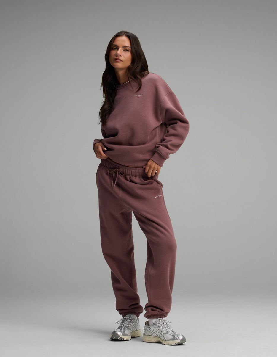 A woman wearing a mauve Cozy Earth Women’s Cityscape Crewneck & Sweatpant Set with white athletic sneakers.