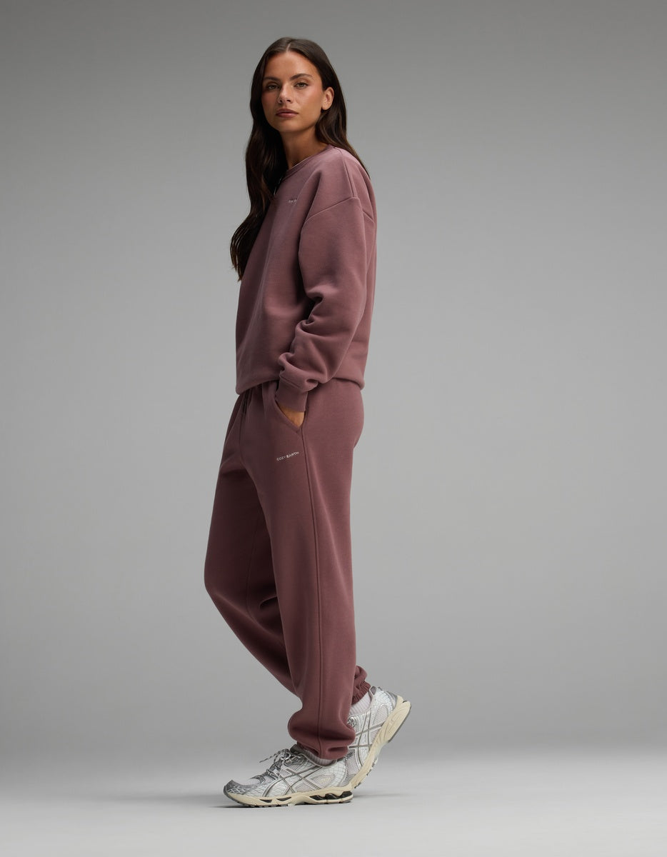 A woman wearing a mauve Cozy Earth Women’s Cityscape Crewneck & Sweatpant Set and silver athletic sneakers.