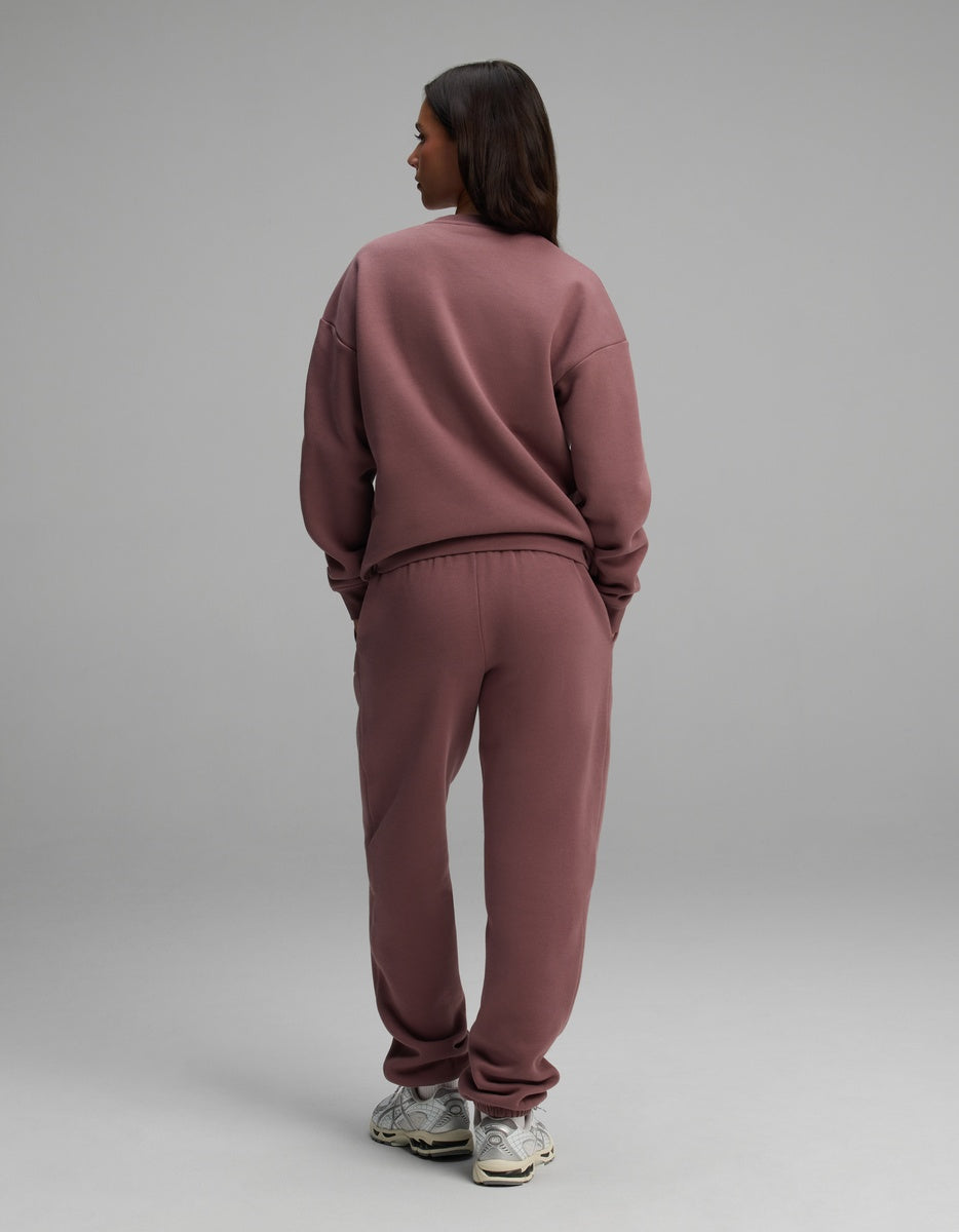 A person stands facing away wearing a dusty rose Cozy Earth Women’s Cityscape Crewneck & Sweatpant Set with white athletic shoes.