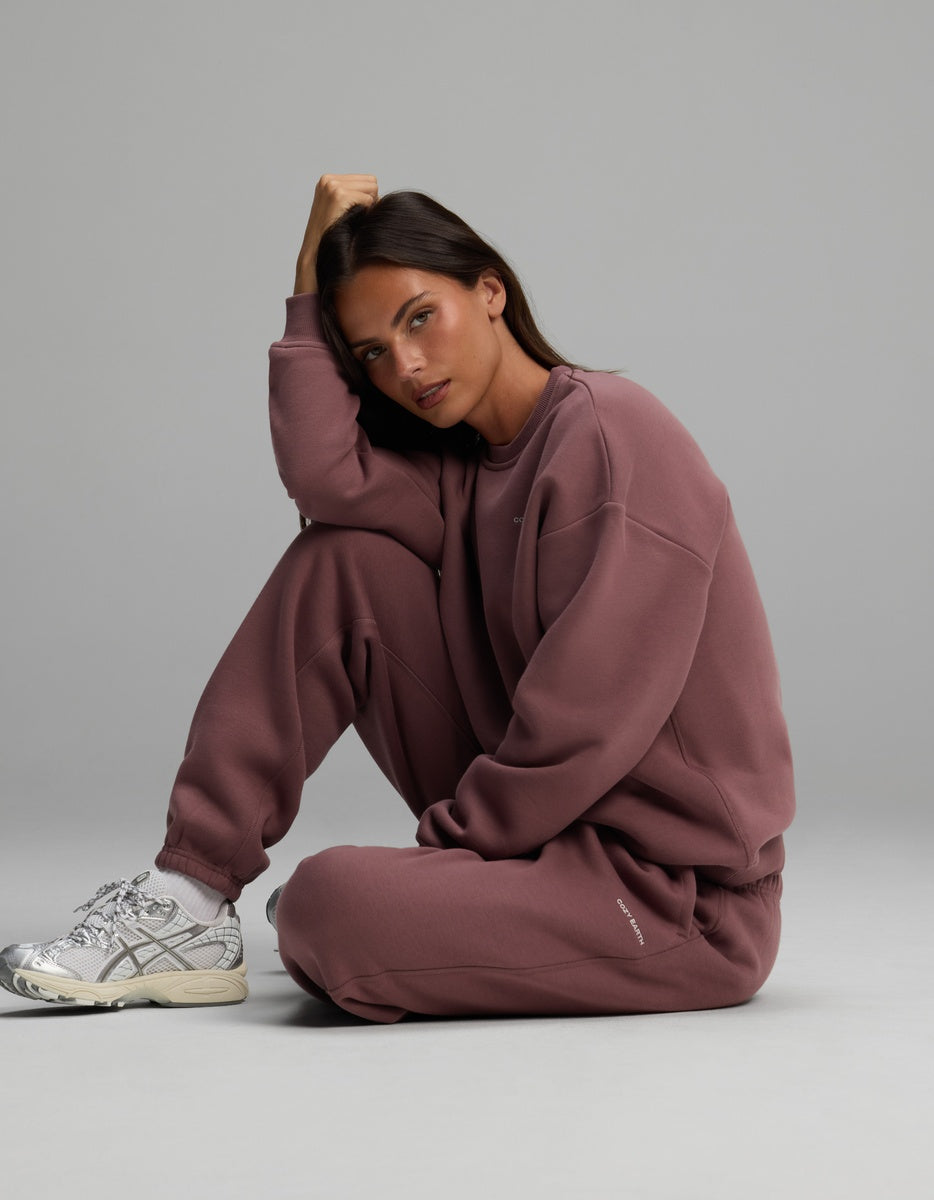 A woman sits on the floor wearing a dusty rose Women’s Cityscape Crewneck & Sweatpant Set with silver athletic sneakers.