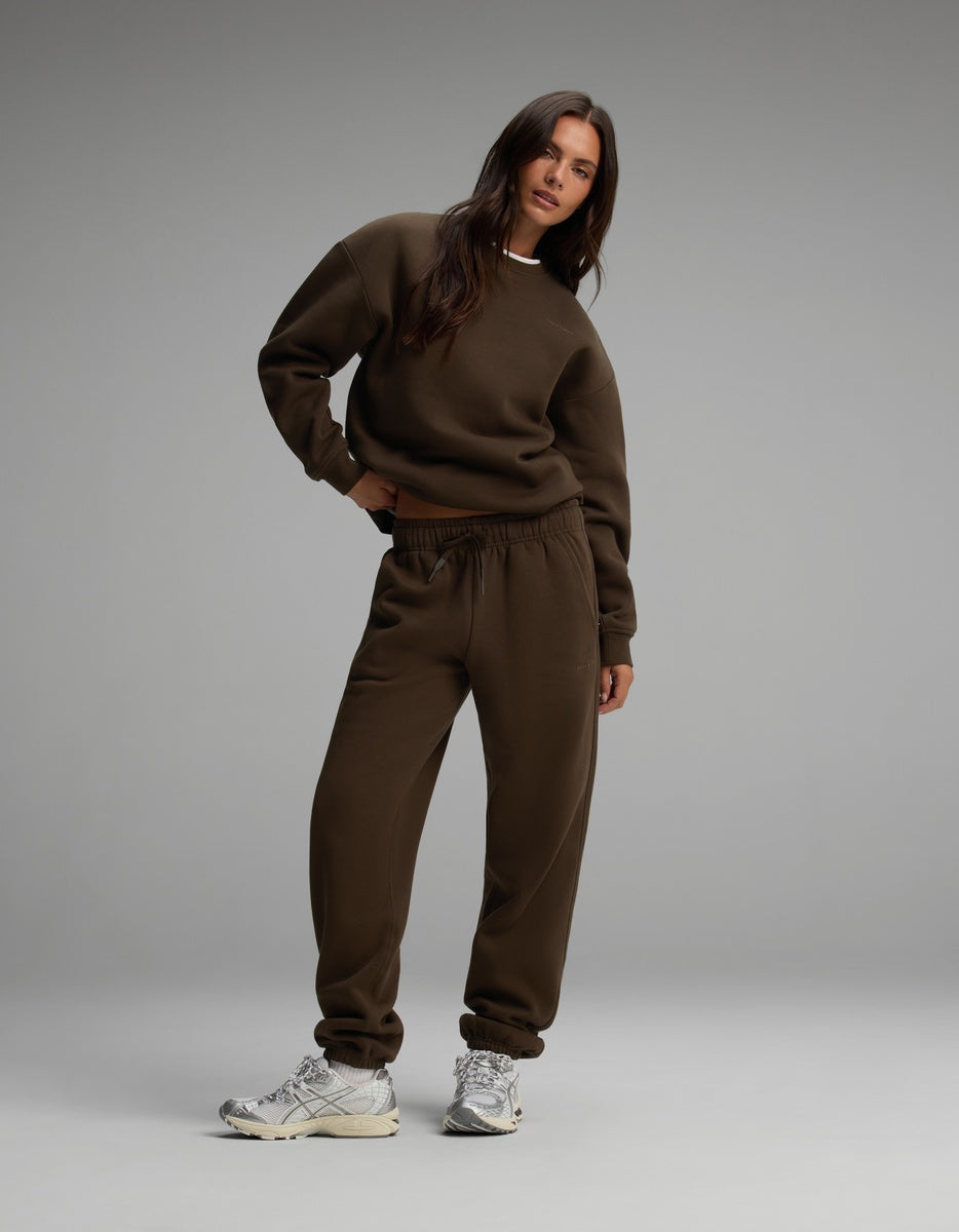 A woman wears a dark brown Cozy Earth Women’s Cityscape Crewneck & Sweatpant Set with metallic silver sneakers.