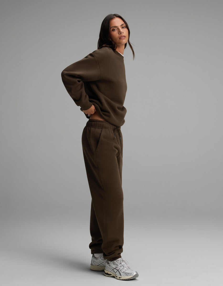 A woman wearing a dark brown Cozy Earth Women’s Cityscape Crewneck & Sweatpant Set with silver athletic sneakers.