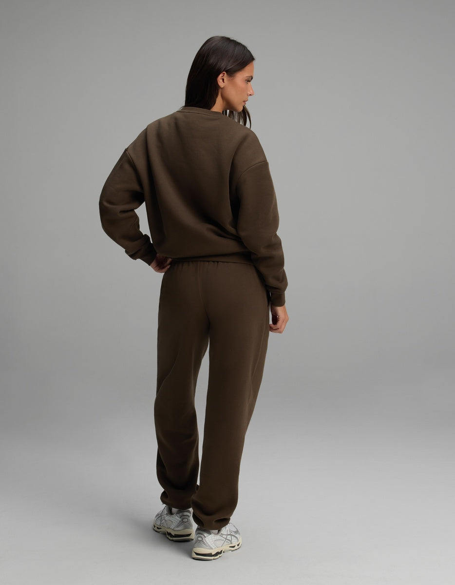 A woman seen from behind, wearing the dark brown Women’s Cityscape Crewneck & Sweatpant Set consisting of a matching crewneck sweatshirt and sweatpants.