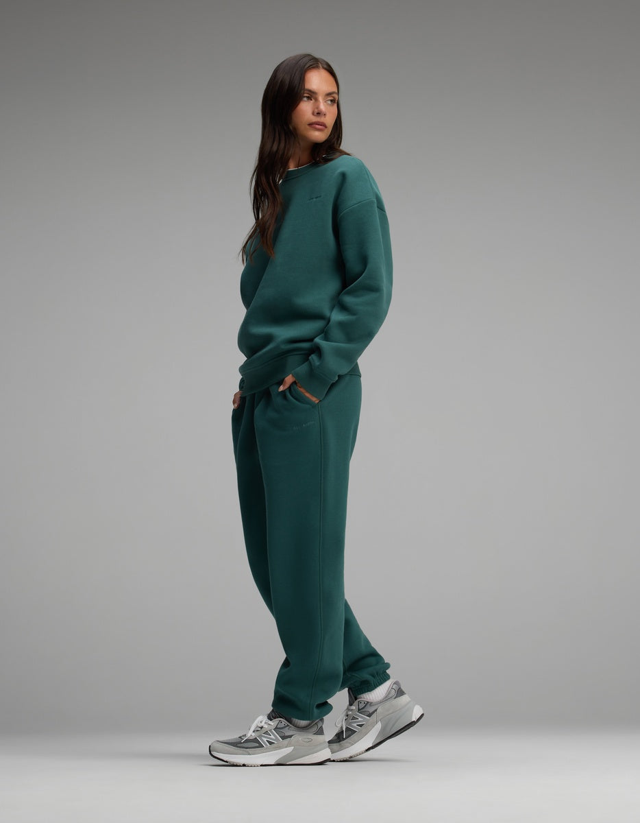 A woman wearing a dark green Cozy Earth Women’s Cityscape Crewneck & Sweatpant Set with grey sneakers.